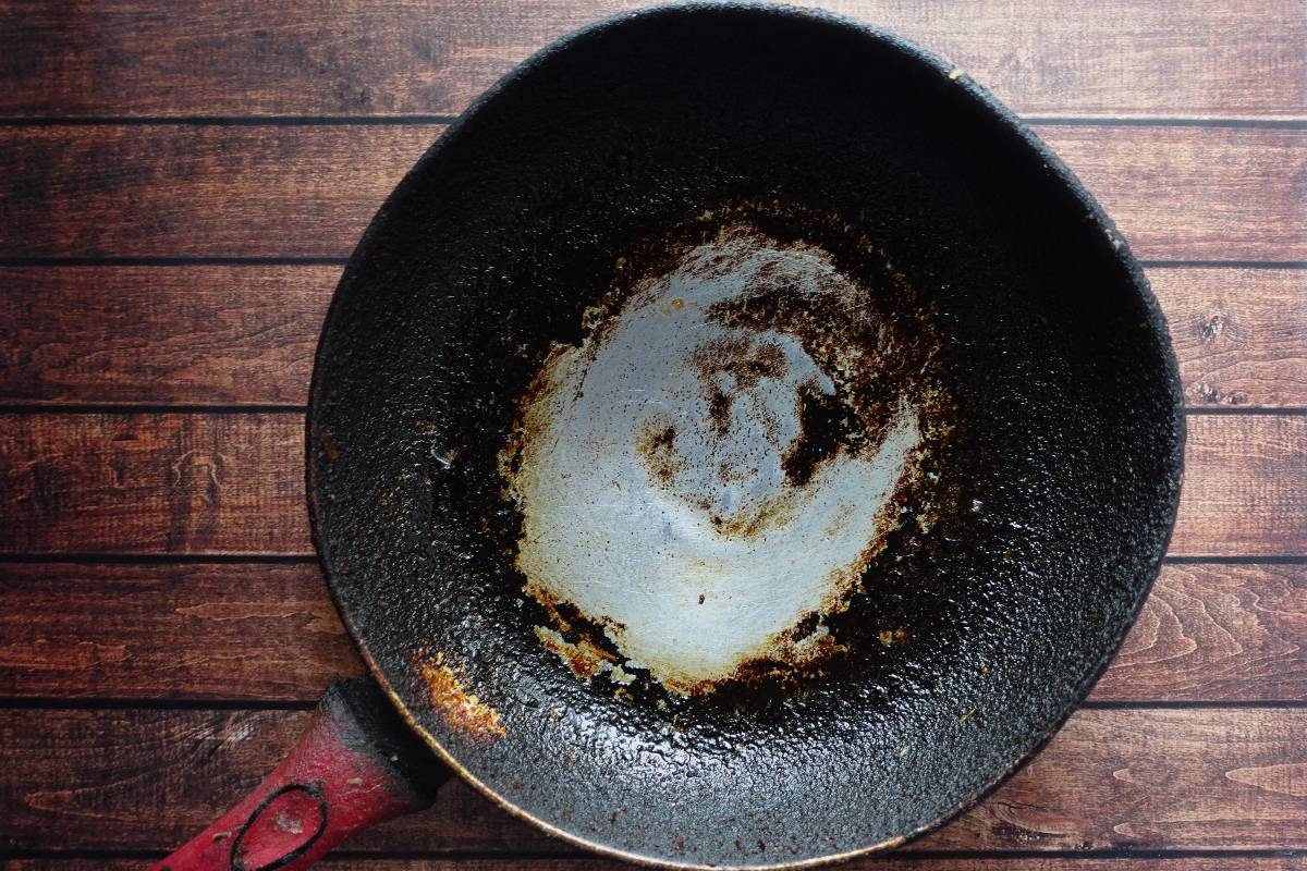 Padella di colore nera con manico in legno, consumata e incrostata
