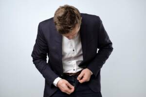 Uomo in elegante completo con giacca e cravatta, con la cerniera dei pantaloni rotta