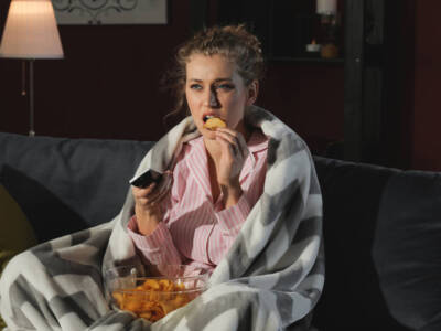 Ragazza sul divano che mangia patatine in pigiama