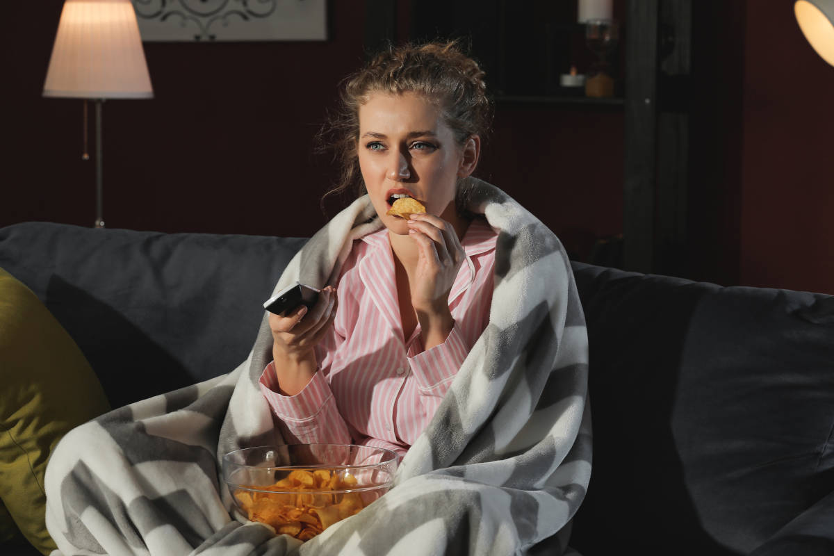 Ragazza sul divano che mangia patatine in pigiama