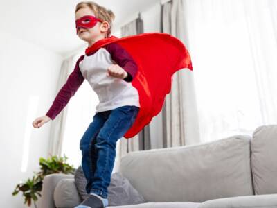 bambino vestito da supereroe che salta dal divano