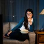 donna sul divano che guarda la televisione con i popcorn