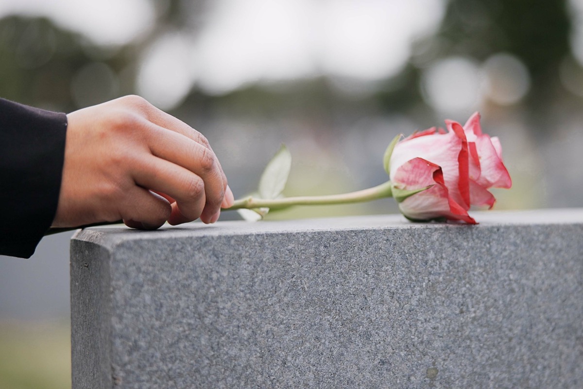 Una figura rende omaggio posando una rosa sulla lapide.