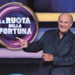 Gerry Scotti con abito blu accanto al logo de "La Ruota della Fortuna"