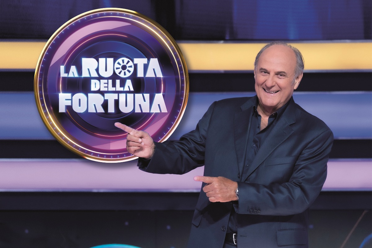 Gerry Scotti con abito blu accanto al logo de "La Ruota della Fortuna"