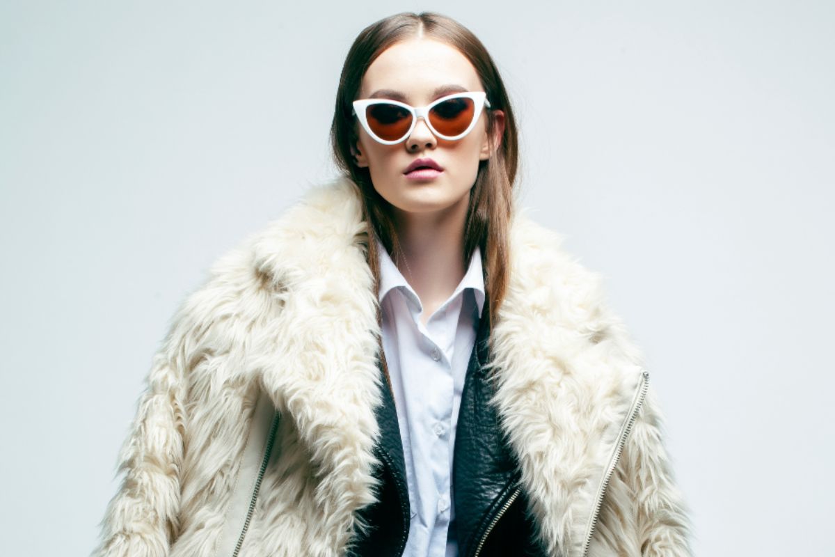 Ragazza con outfit di tendenza: occhiali da sole, giacca di pelle e pelliccia.