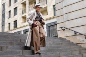 Donna in outfit elegante, pantaloni sartoriali e cappotto lungo, scende le scale in una grande città.