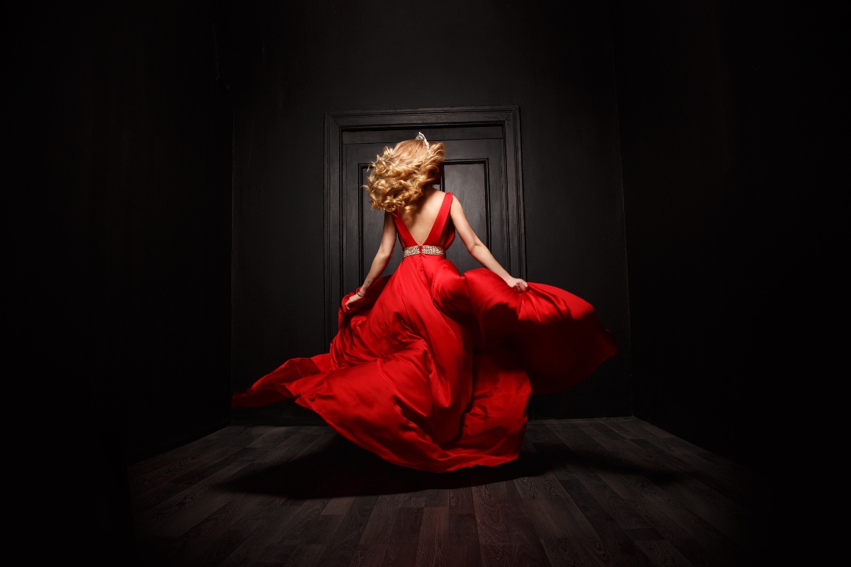 Donna in abito rosso elegante con gonna ampia, mentre corre via di spalle.