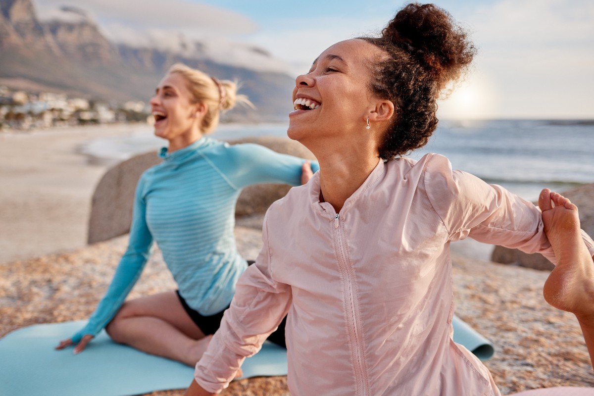 Ragazze sorridenti praticano yoga in spiaggia.