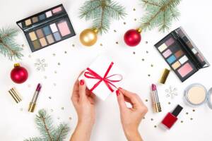 Makeup festivo: prodotti sul tavolo bianco, al centro un pacchetto regalo di Natale.