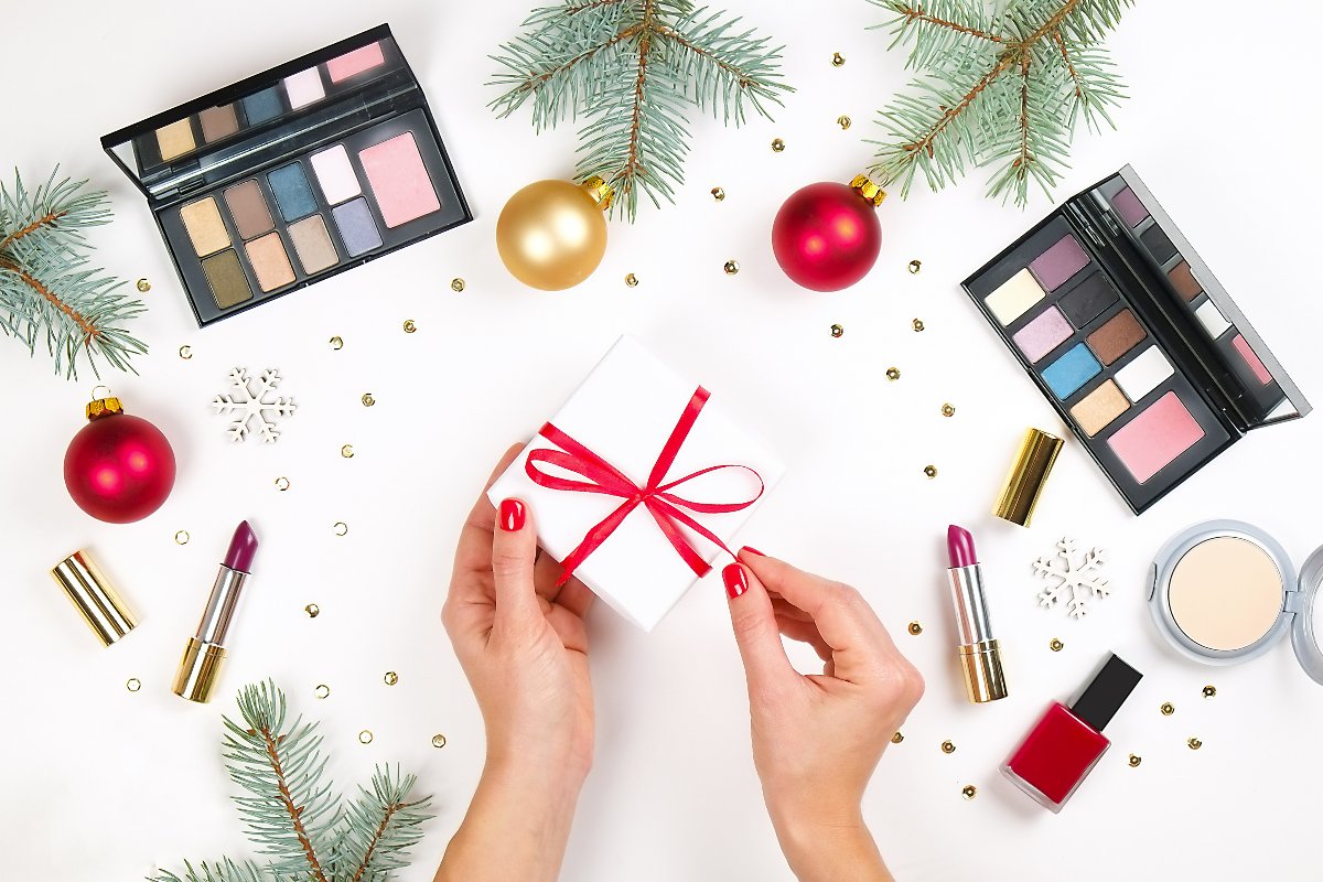 Makeup festivo: prodotti sul tavolo bianco, al centro un pacchetto regalo di Natale.