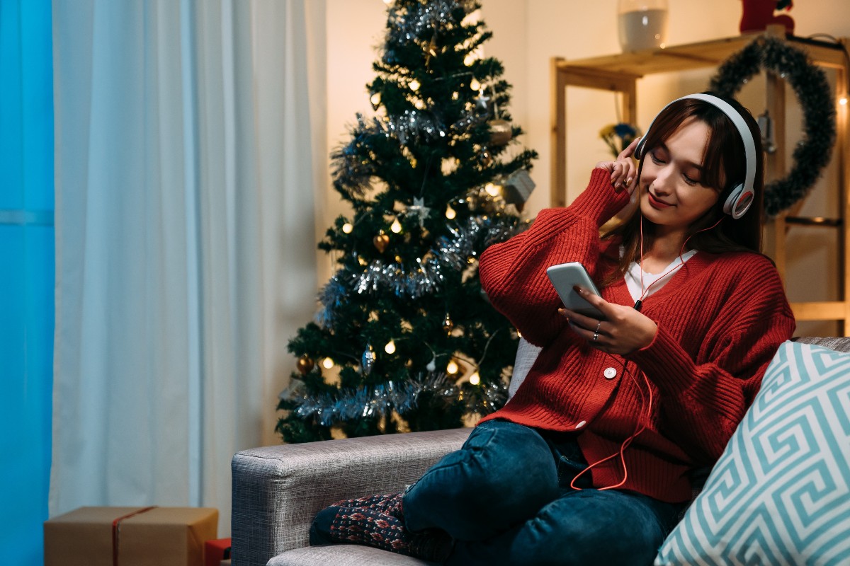 Ragazza ascolta musica con l'albero di Natale alle spalle