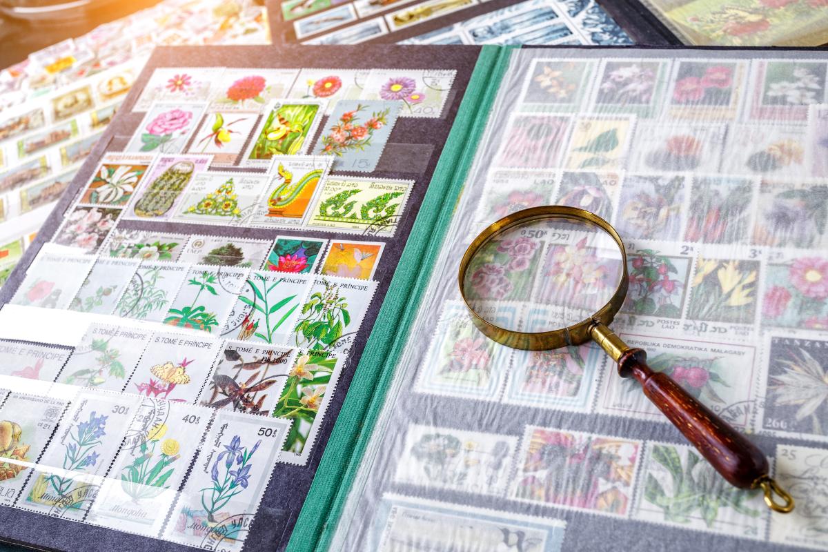 Album di francobolli tematici con illustrazioni floreali, affiancato da una lente d’ingrandimento utilizzata per analizzare dettagli e autenticità