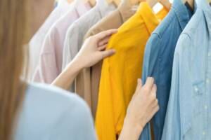 Shopping: una donna seleziona camicie vivaci e colorate tra gli scaffali del negozio.