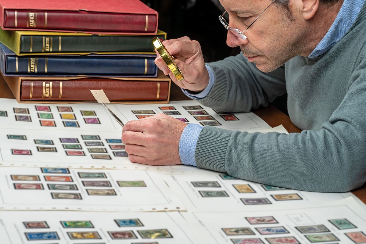 Un collezionista di francobolli osserva attentamente una rara emissione con lente d’ingrandimento, immerso tra album storici e schede filateliche