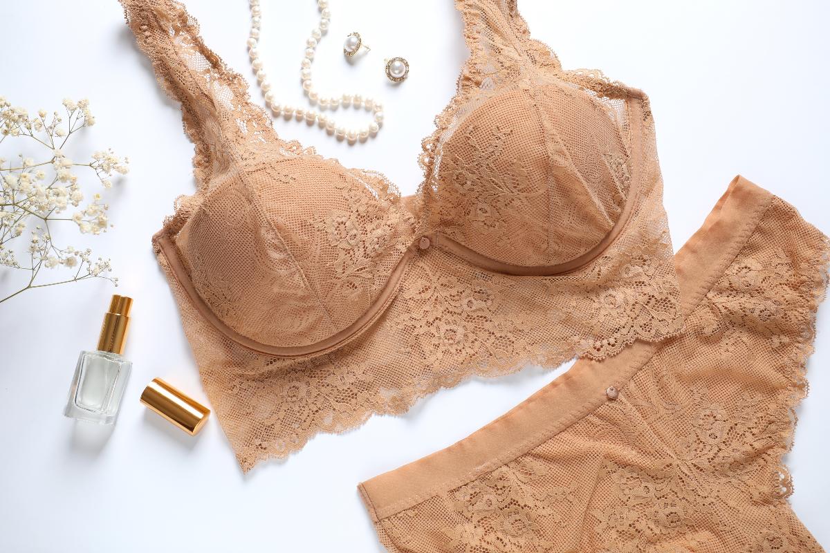 Set elegante: completo intimo color carne su fondo bianco con profumo e gioielli.