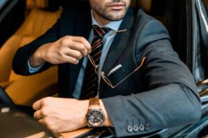 Stile alla guida: uomo elegante al volante con orologio e occhiali in evidenza.