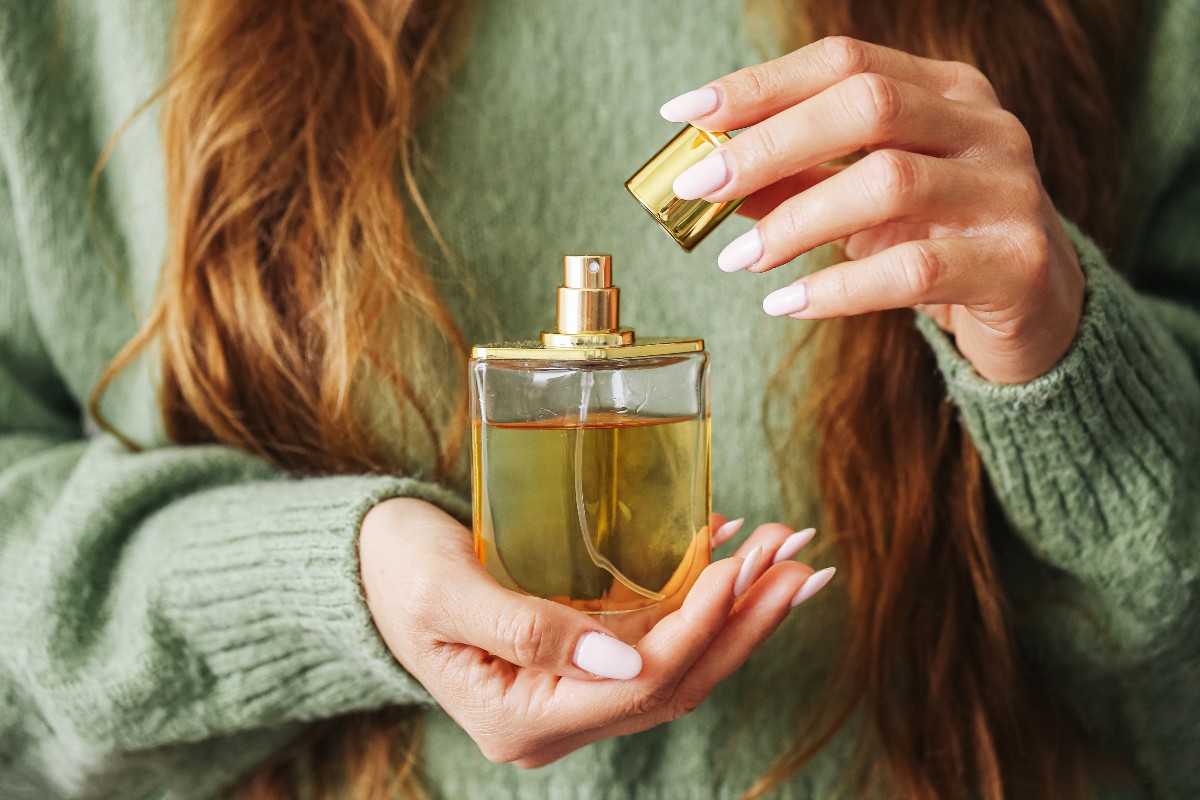 Una ragazza con maglione verde tiene tra le mani un flacone di profumo.
