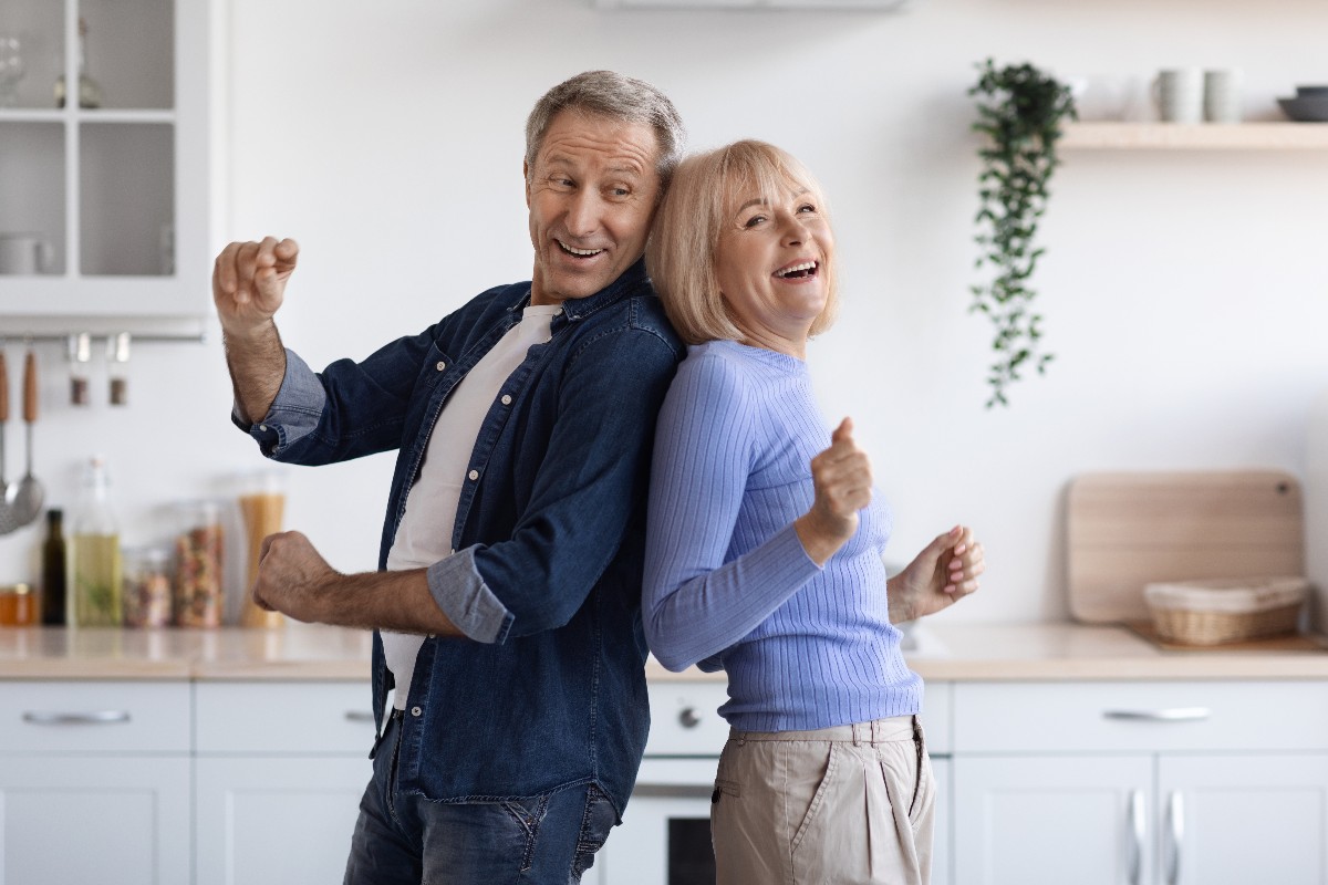 Una coppia felice che si diverte a ballare schiena contro schiena al centro della cucina.