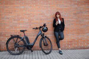 Una e-bike nera appoggiata a una parete con una ragazza in piedi accanto alla bicicletta.