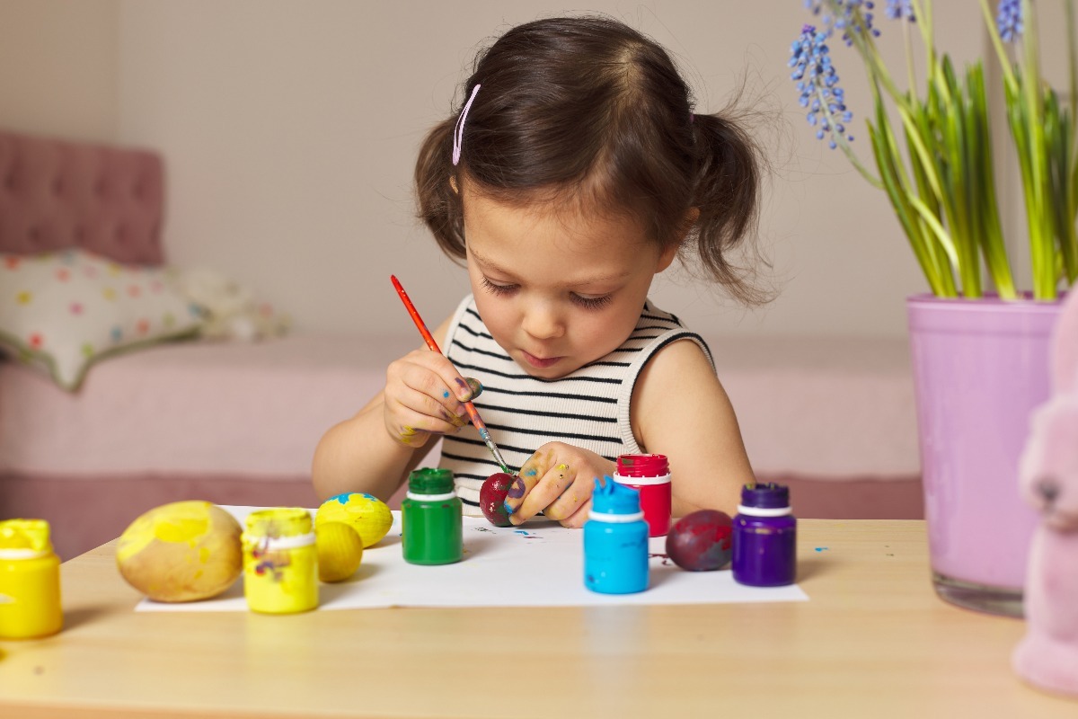 Una bambina con i codini dipinge le uova di Pasqua