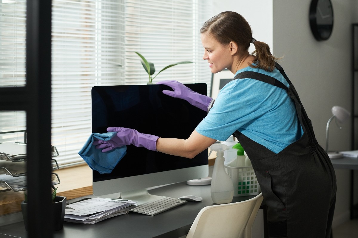 Una donna con i guanti lilla pulisce lo schermo del PC