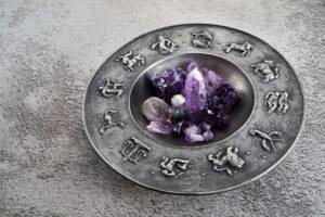 Piatto metallico con simboli zodiacali in rilievo e decorazione di cristalli viola.