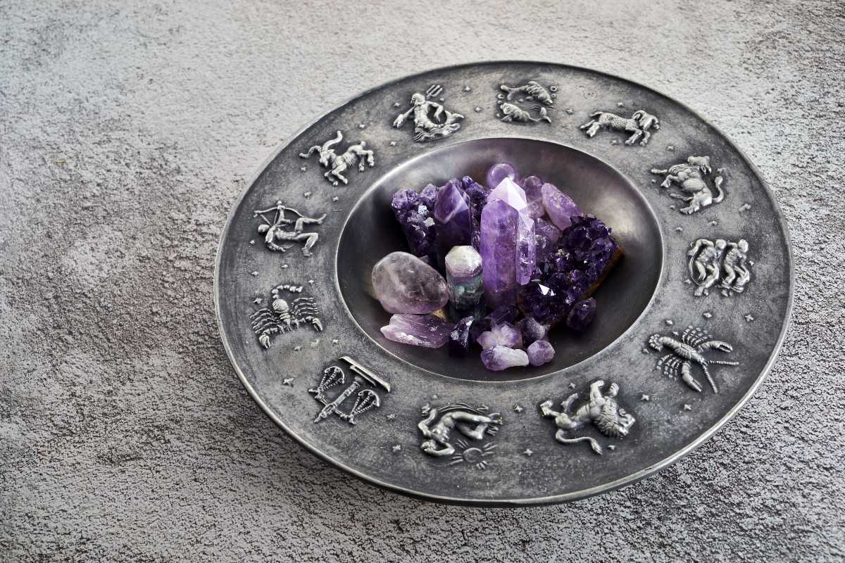 Piatto metallico con simboli zodiacali in rilievo e decorazione di cristalli viola.