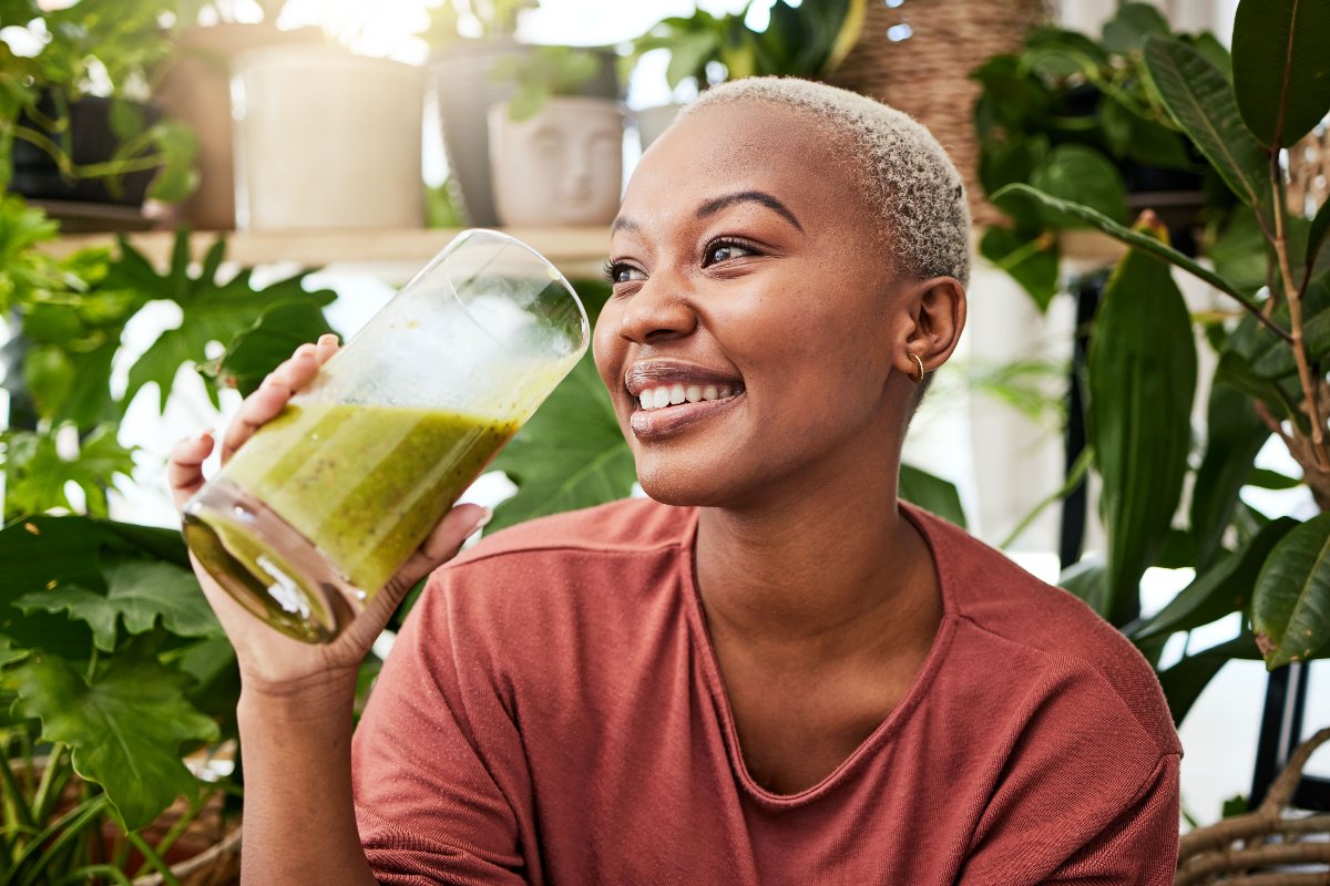 Ragazza sorridente mentre beve un frullato verde.