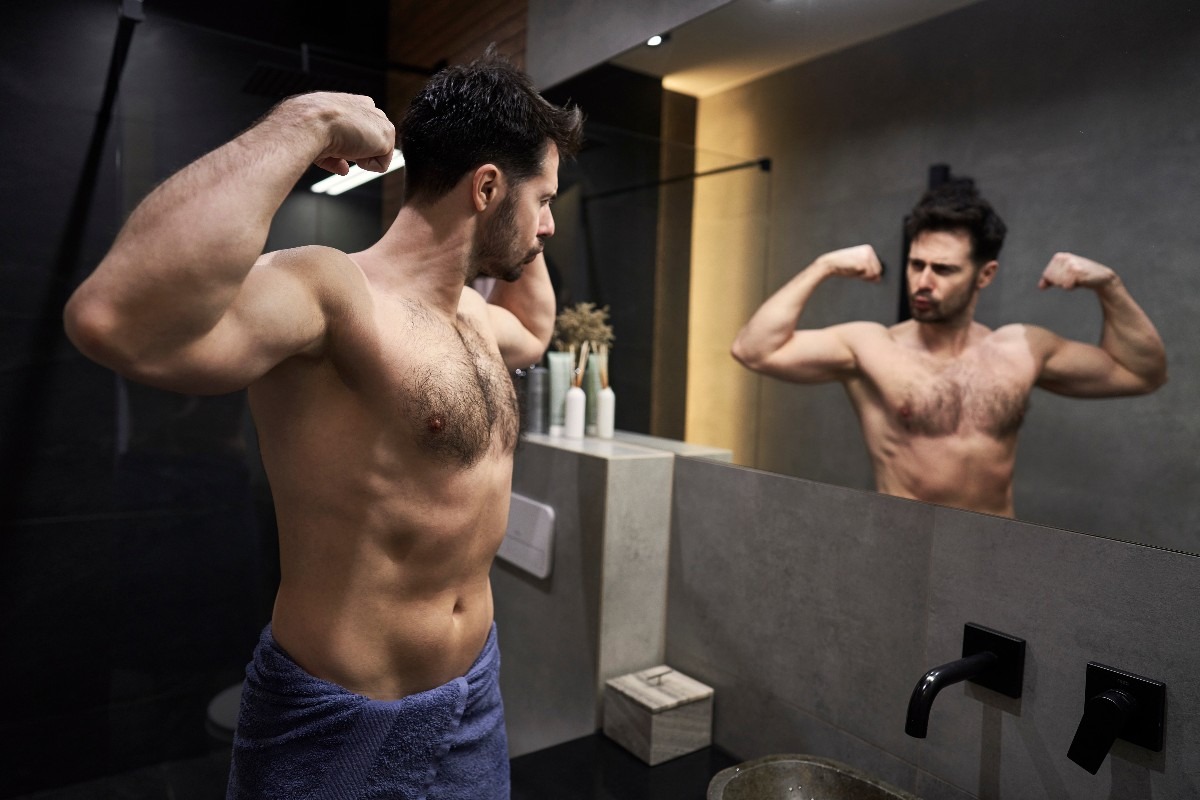 Uomo si specchia al bagno mostrando i muscoli
