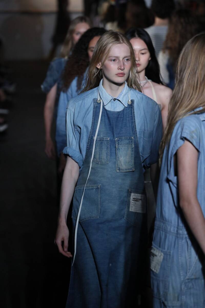 Una modella sfila in passerella con un grembiule di jeans rivisitato come accessorio di alta moda.