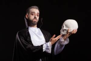 Uomo affascinante travestito da Dracula con denti da vampiro mentre tiene un teschio umano