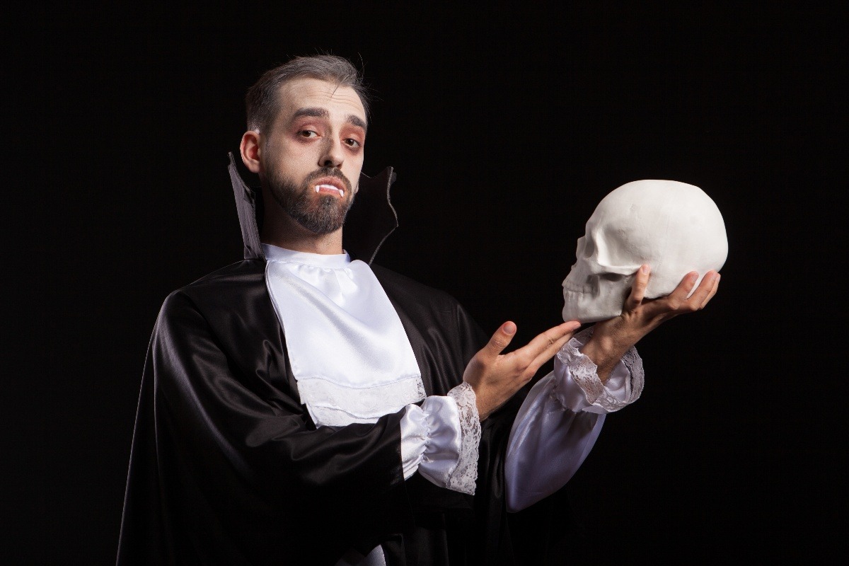 Uomo affascinante travestito da Dracula con denti da vampiro mentre tiene un teschio umano