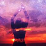 Sagoma di una giovane donna in piedi con le mani protese verso l’alto a toccare le stelle sulla riva del mare al tramonto, sullo sfondo dello spazio e del cielo stellato
