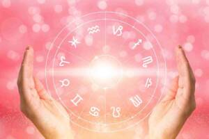 Due mani circondano i dodici segni zodiacali su uno sfondo rosa, evocando il legame tra astrologia, oroscopo e destino