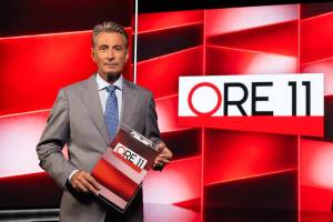 Milo Infante in giacca e cravatta conduce Ore 11