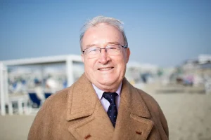 Mario Giuliacci con un cappotto beige in spiaggia
