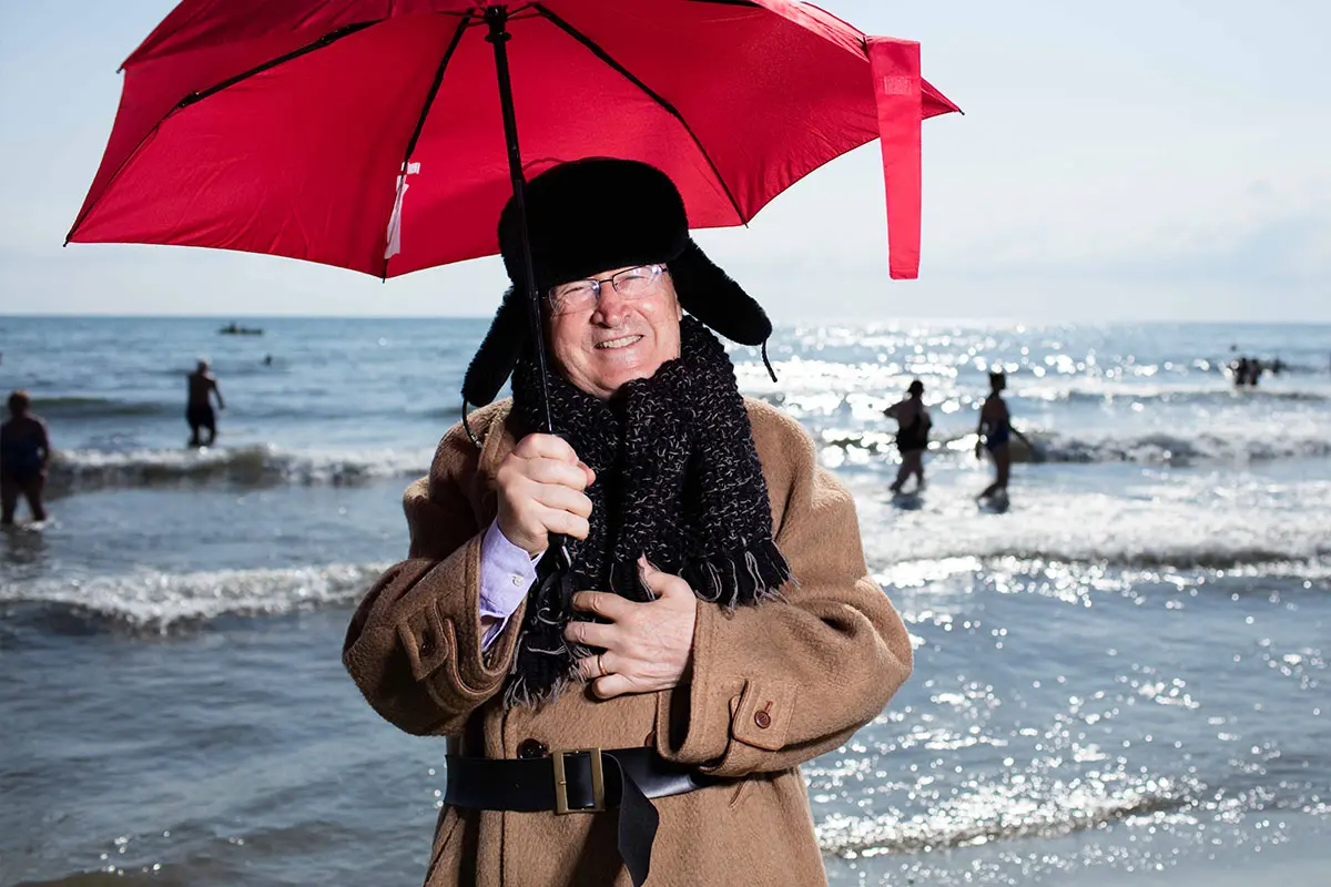 Mario Giuliacci con un ombrello rosso e il cappotto al mare